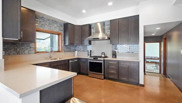 A modern kitchen with dark cabinetry, a central island, and a large stove. - Cloud-Break Ridge | Pool, Spa - Epic Mountain Views (Malibu)