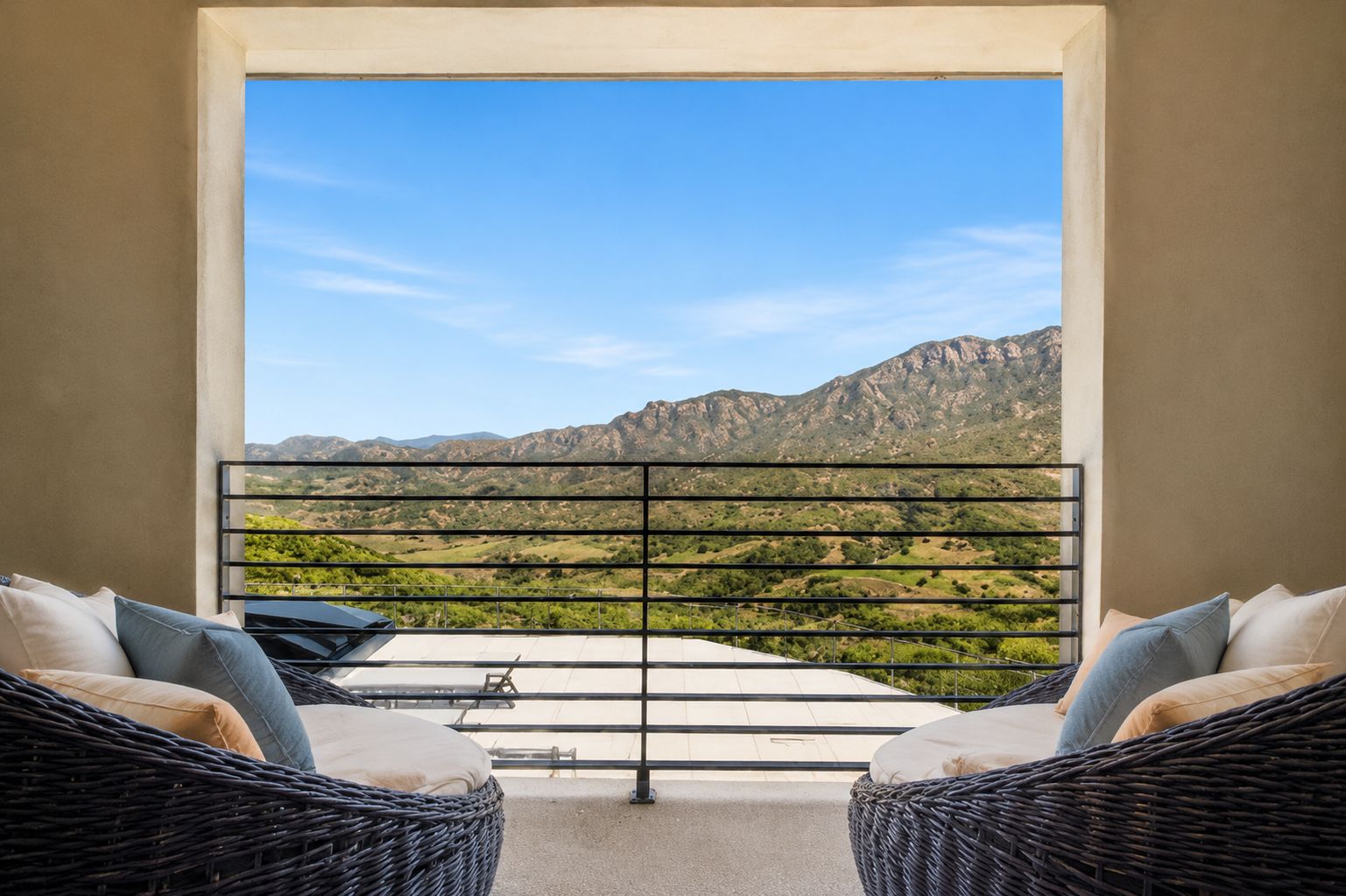 A balcony with wicker furniture and a view of a mountainous landscape.