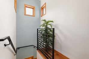 Una escalera con barandilla de madera, una reja de metal negro y una planta en maceta.