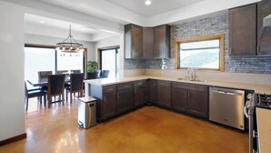 A modern kitchen with dark cabinets, a stone backsplash, and a large island. - Cloud-Break Ridge | Pool, Spa - Epic Mountain Views (Malibu)