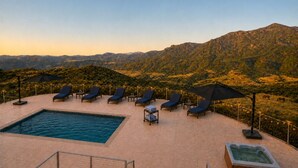 A rooftop pool area with lounge chairs and umbrellas, overlooking a mountainous landscape.