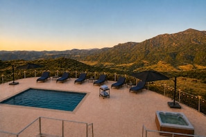 A rooftop pool area with lounge chairs and umbrellas, overlooking a mountainous landscape.
