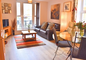 Un salon avec un canapé, une table en verre, un téléviseur et une fenêtre avec des rideaux.