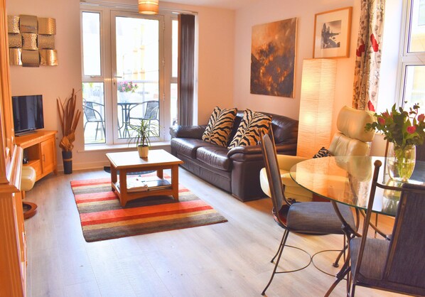A living room with a sofa, a glass table, a TV, and a window with curtains. - City Centre 2 Bedroom Ground Floor Flat with Parking (Chichester)
