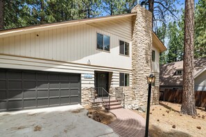 A two-story house with a stone chimney, a garage, and a brick pathway leading to the front door. - Sky Krest (Big Bear Lake)