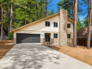 A two-story house with a stone chimney, a garage, and a driveway leading to the entrance. - Sky Krest (Big Bear Lake)