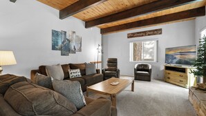 A cozy living room with a wooden ceiling, a sofa set, a coffee table, and a TV stand with a plant. - Sky Krest (Big Bear Lake)