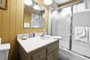 A bathroom with a white sink, a mirror, and a shower with frosted glass doors. - Sky Krest (Big Bear Lake)