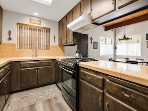 A kitchen with dark wooden cabinets, a gas stove, a sink, and a window with blinds. - Sky Krest (Big Bear Lake)
