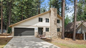A two-story house with a stone chimney, a garage, and a front yard with trees. - Sky Krest (Big Bear Lake)