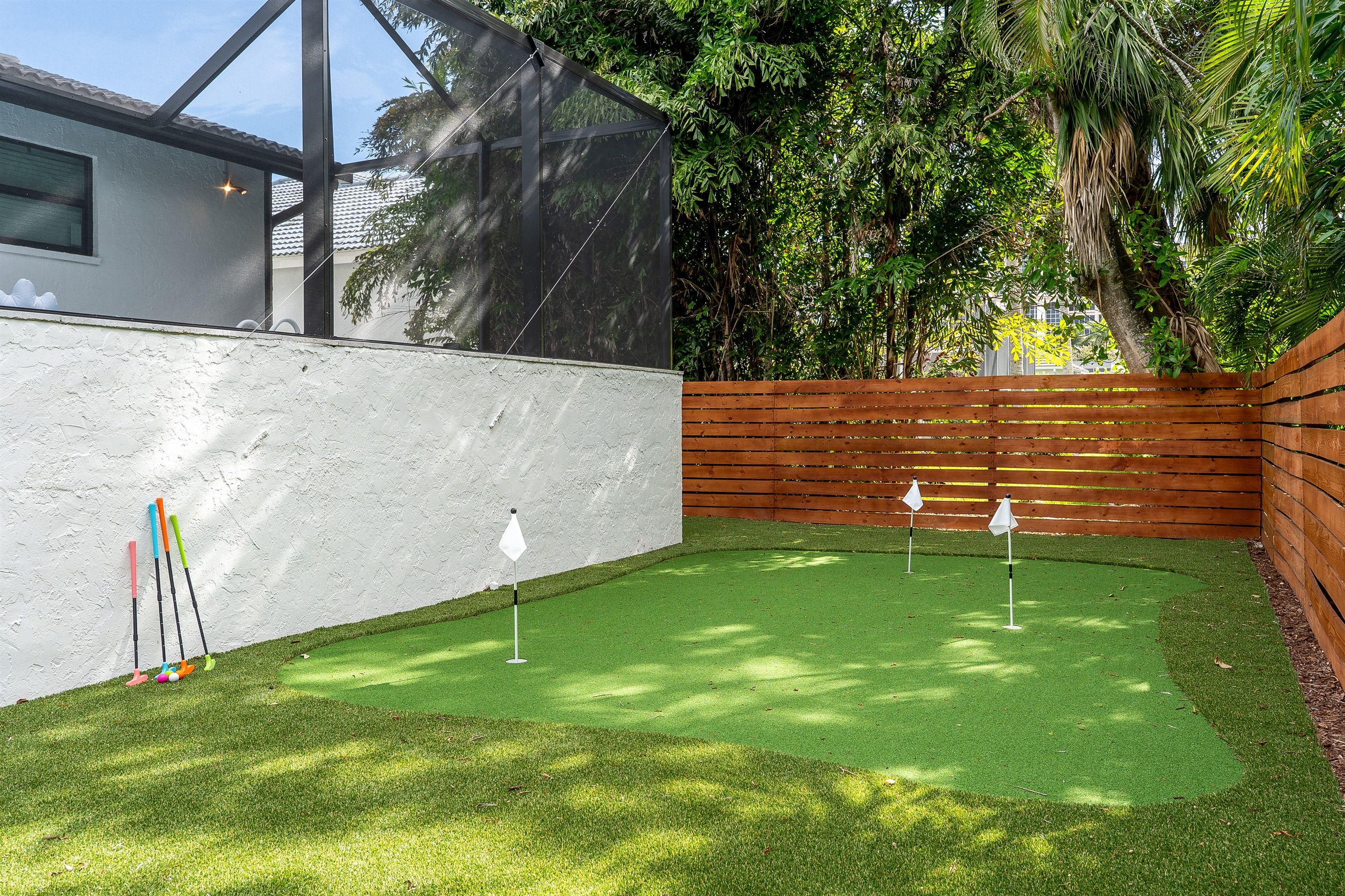 Un patio con césped artificial, una valla de madera y una pared blanca.