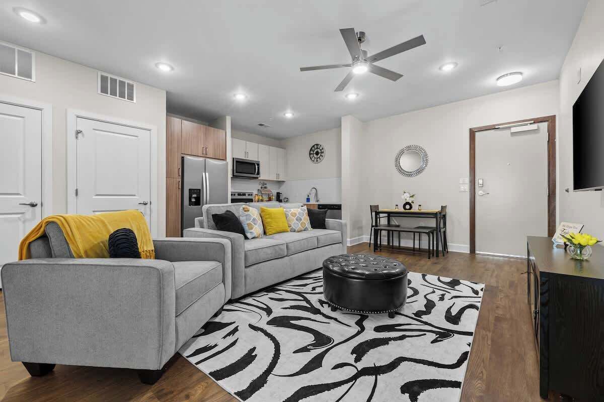 Un salon moderne avec un canapé gris, un pouf noir et un tapis à motifs zébrés.