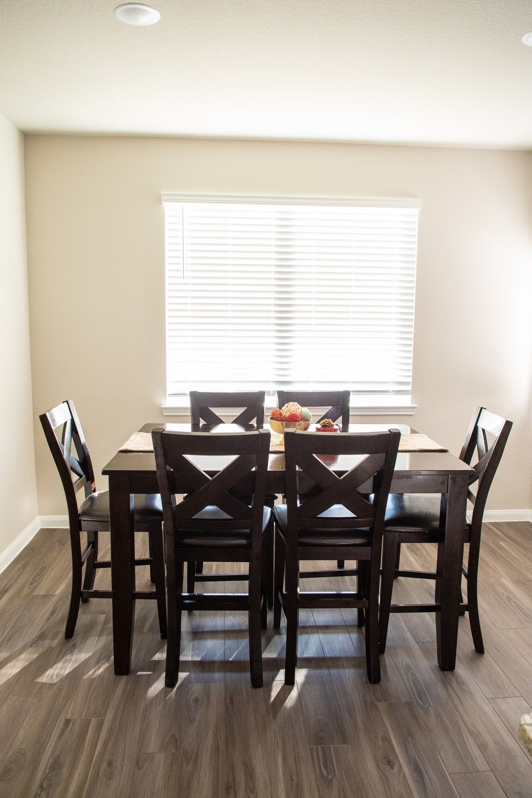 A dining area with a table and chairs, a window with blinds, and a wooden floor.