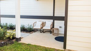 A covered patio area with two wicker chairs and a small round table, surrounded by a garden with plants and a black circular mat. - Spacious 4-bedroom house in beautiful Conroe with King Suite (Conroe)