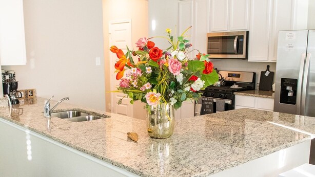A modern kitchen with white cabinets, a granite countertop, a stainless steel refrigerator, and a vase of flowers on the island. - Spacious 4-bedroom house in beautiful Conroe with King Suite (Conroe)