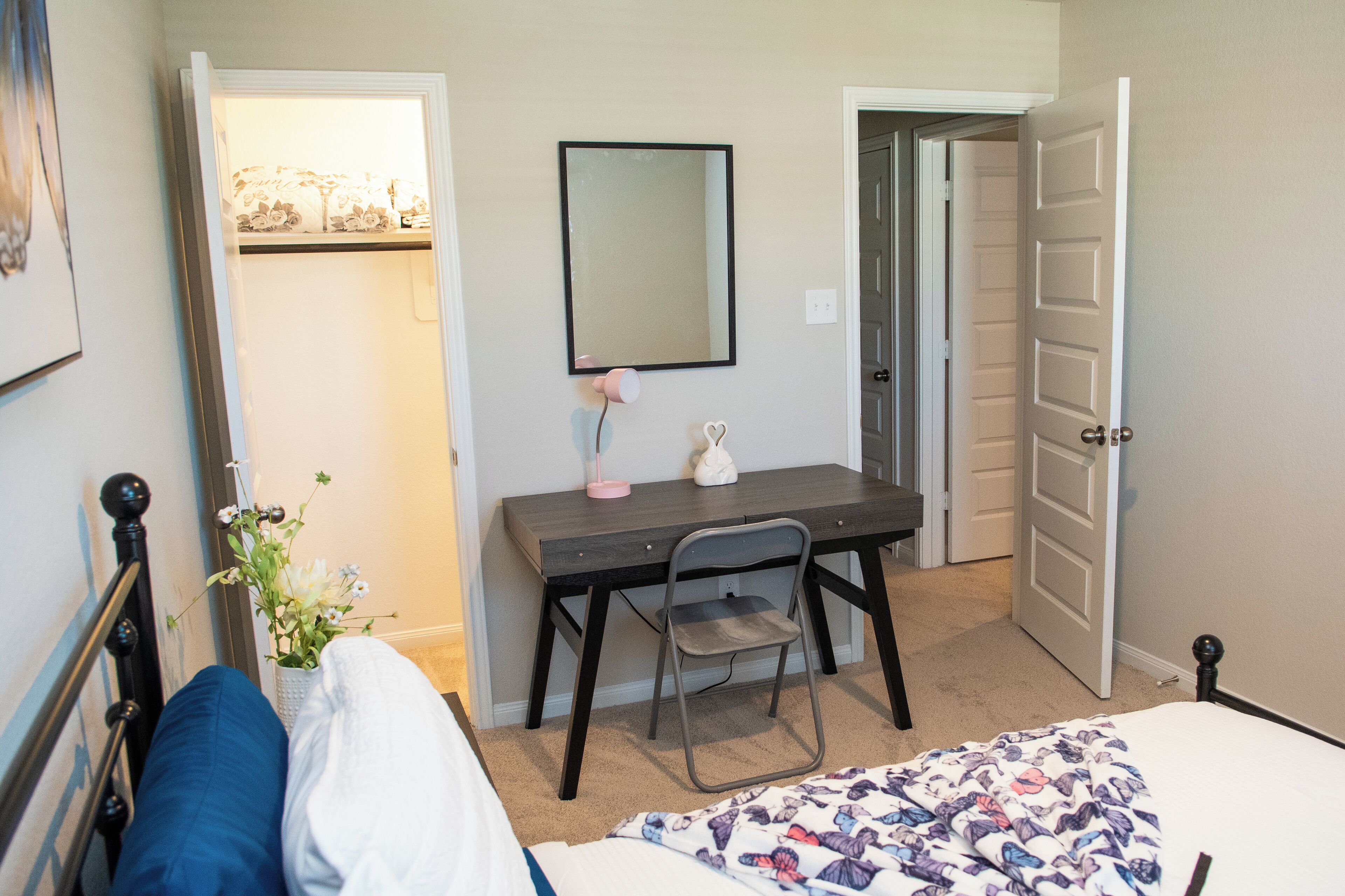 A bedroom with a bed, a desk, a chair, a dresser, and a door.
