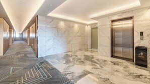 Een moderne hotelgang met marmeren vloer, een prullenbak en een lift.