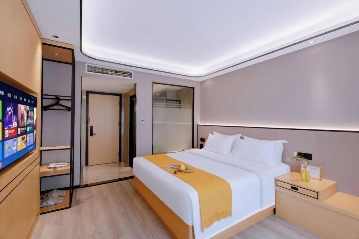 Moderni hotellihuone, jossa on sänky, yöpöytä ja seinälle asennettu televisio.