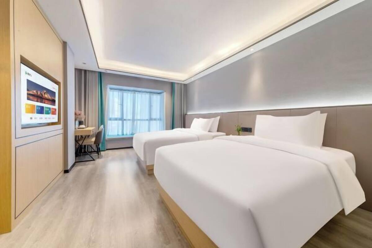Hotellihuone, jossa on kaksi sänkyä, työpöytä ja suuri ikkuna.
