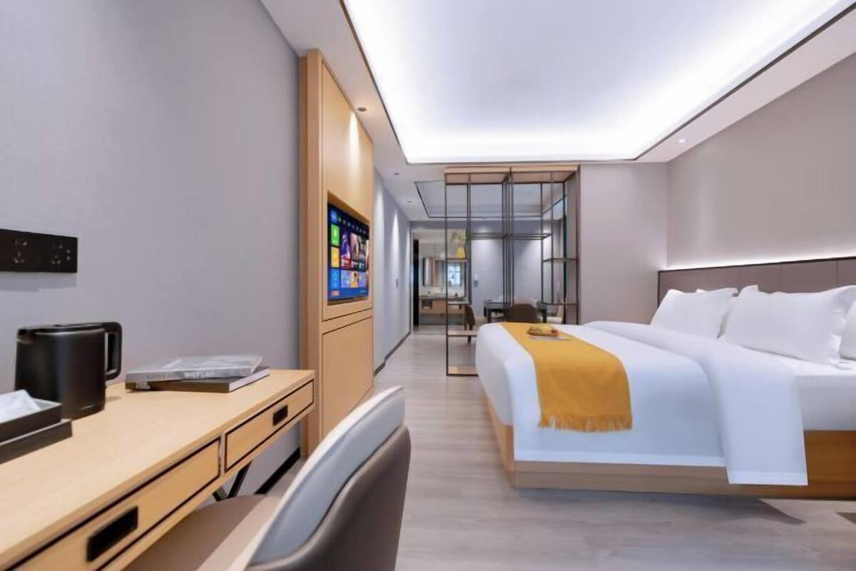 Moderni hotellihuone, jossa on sänky, työpöytä, tuoli ja seinälle asennettu digitaalinäyttö.