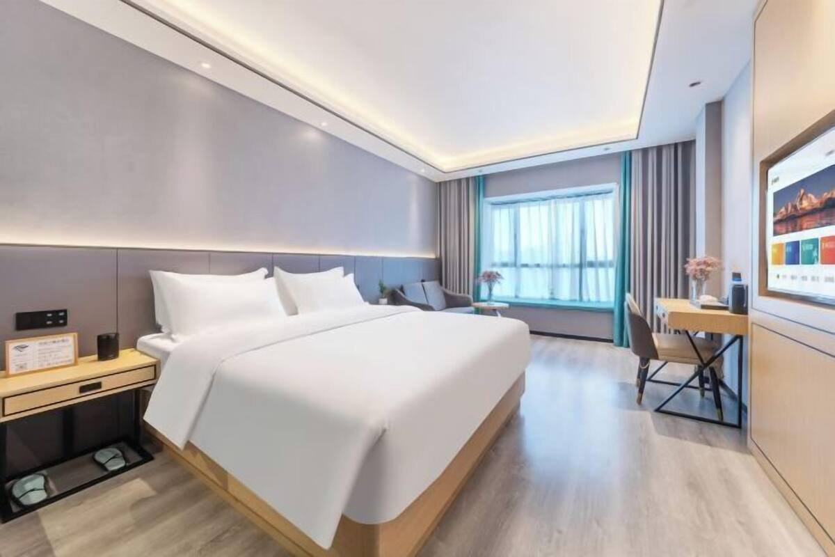 Moderni hotellihuone, jossa on suuri sänky, yöpöytä ja työpöytä tuolilla.