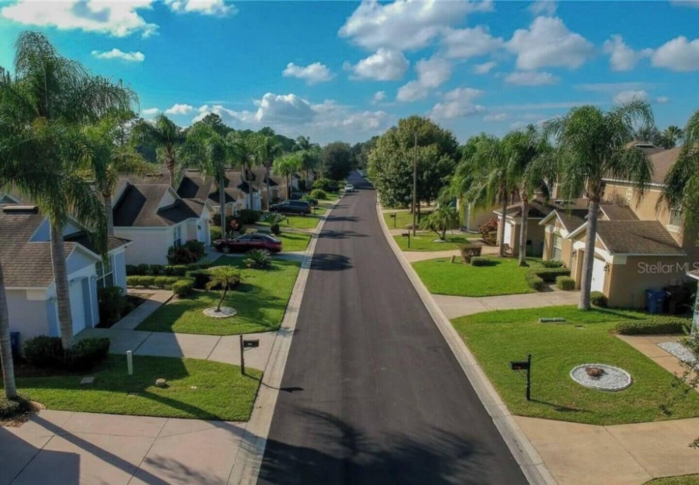A residential street with single-family homes, well-maintained lawns, and a clear sky.