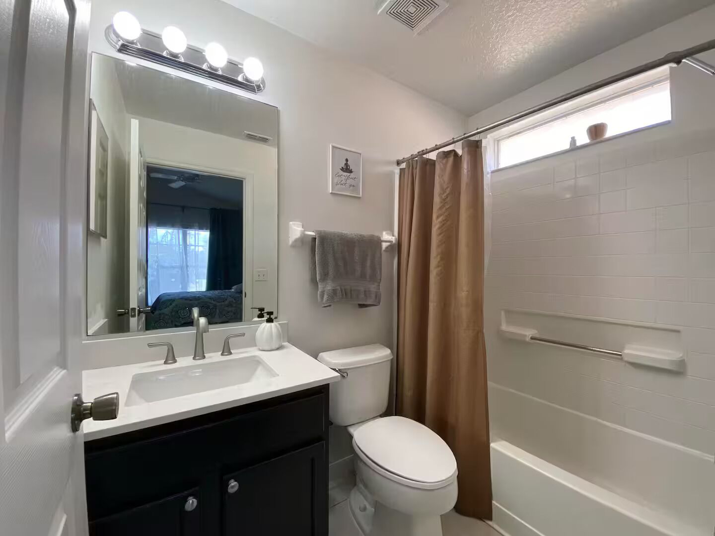 Un bagno con un lavabo bianco, un water, uno specchio illuminato, un porta asciugamani e uno spazio doccia.