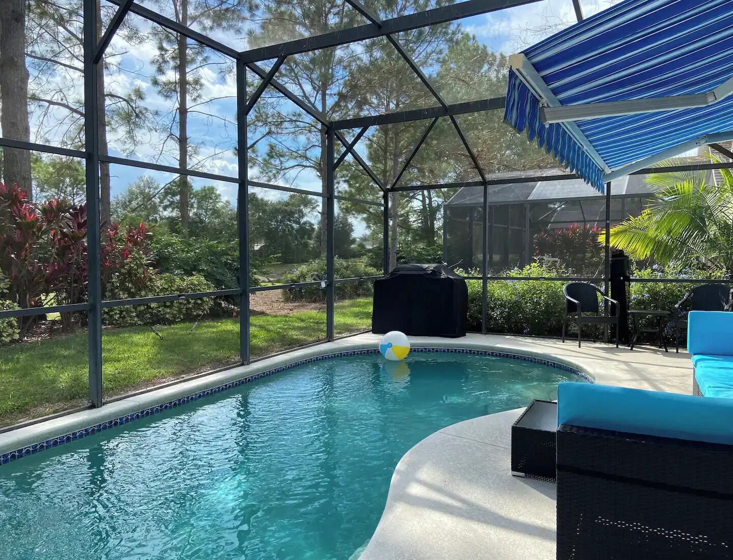 Una piscina con cerramiento de vidrio, rodeada de vegetación y mobiliario exterior.