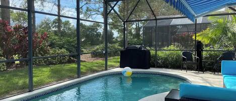Una piscina con cerramiento de vidrio, rodeada de vegetación y mobiliario exterior.