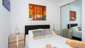 Ein modernes Schlafzimmer mit einem großen Bett, zwei Nachttischen, einem Spiegel und Kunstwerken an der Wand.