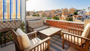 Ein Balkon mit einer Couch, Stühlen und einem Tisch, mit Blick auf ein Wohngebiet mit Gebäuden.
