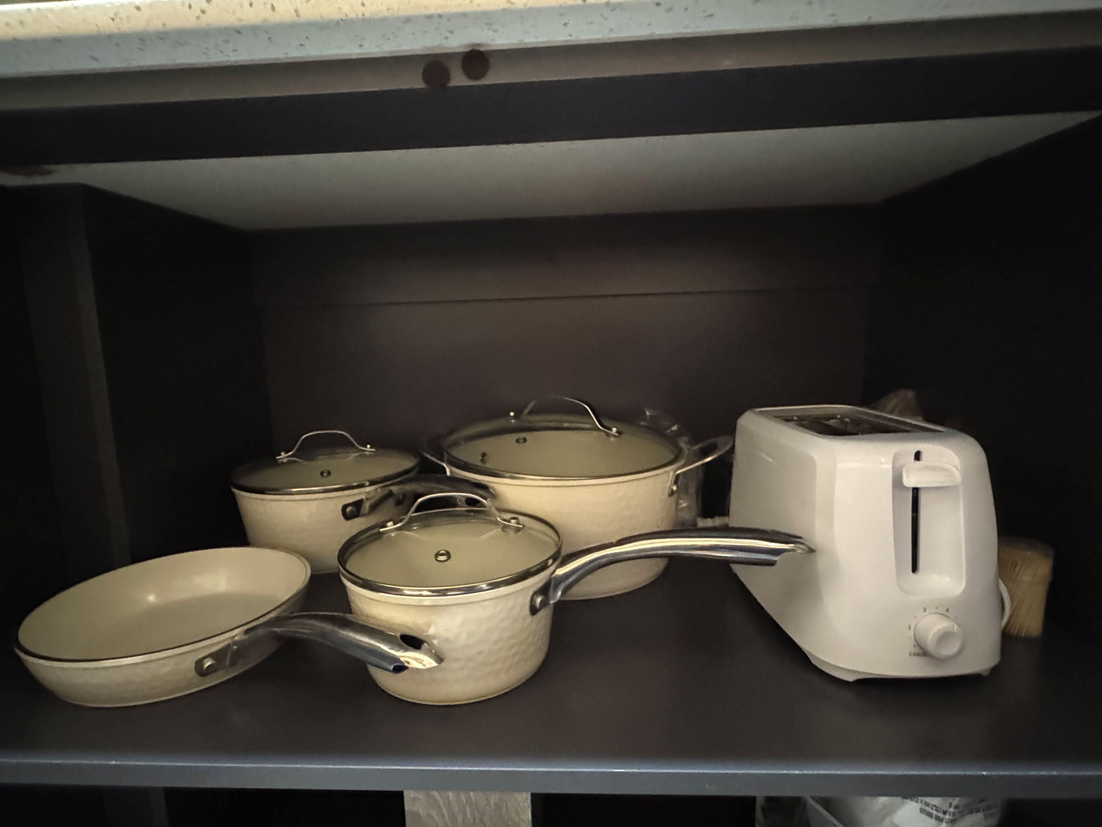 A kitchen shelf with pots, pans, and a toaster.