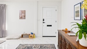 En moderne stue med en hvid dør, et lille træsidebord, en potteplante og et indrammet billede på væggen.