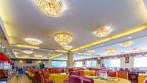 Un comedor amplio con varias mesas redondas y sillas, decorado con grandes candelabros y manteles amarillos.