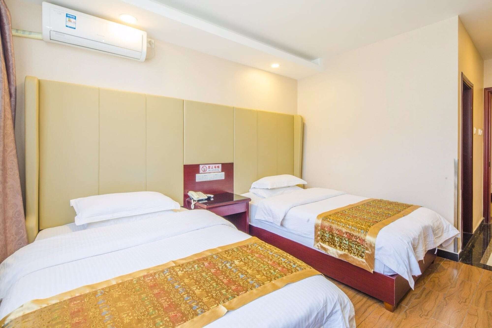 Een hotelkamer met twee bedden, een nachtkastje met een telefoon en een airconditioning aan de muur.