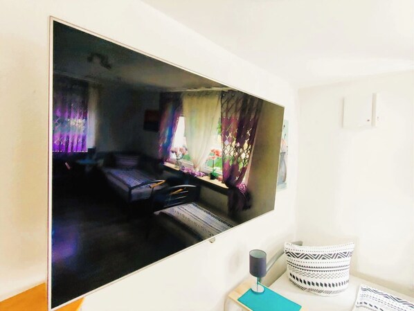 Una stanza con un letto, una finestra con tende, un tavolino con una lampada e una TV a muro.