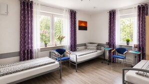 Una habitación con dos camas individuales, un escritorio, sillas, una ventana con cortinas y una planta.