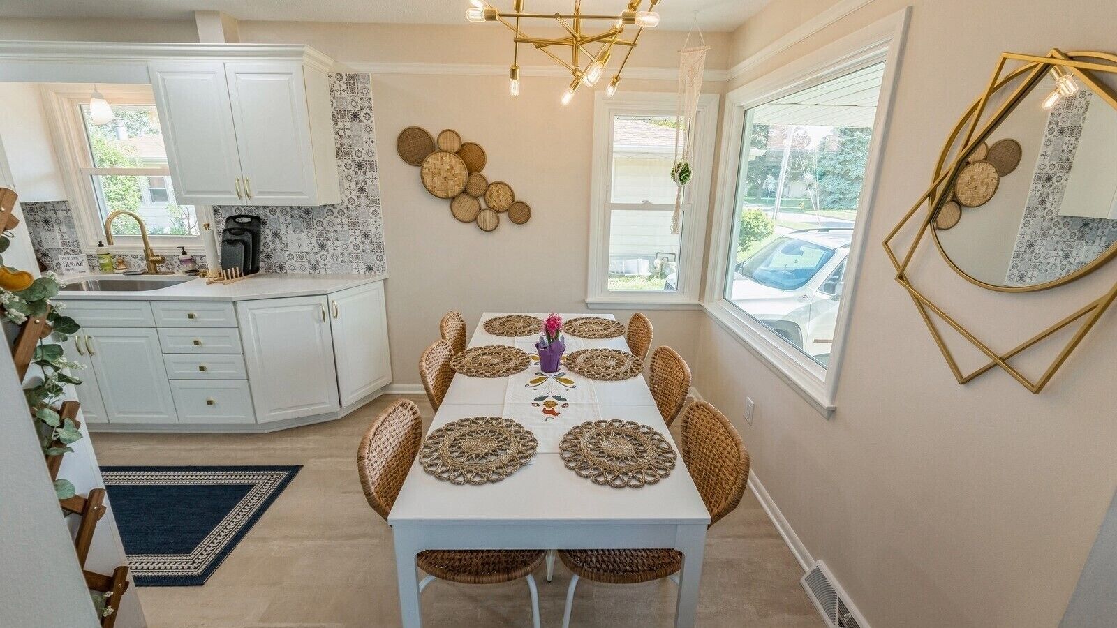 A dining area with a white table, woven placemats, wicker chairs, and a chandelier.