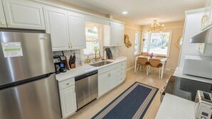 A modern kitchen with white cabinetry, stainless steel appliances, a dishwasher, and a dining area with wicker chairs.