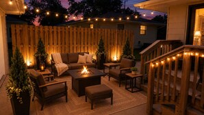 An outdoor patio with a fire pit, seating, and string lights.