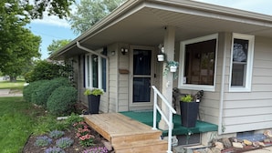 A house with a front porch, a small wooden bench, potted plants, and a stone pathway leading to the door.