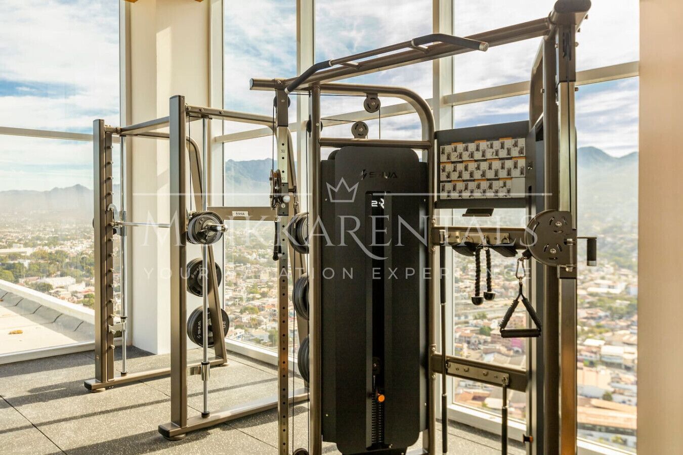 Una palestra con vista panoramica sulla città, dotata di attrezzature per sollevamento pesi e un'ampia vetrata.