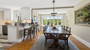 Una cocina moderna con armarios blancos, una zona de comedor con una gran mesa de madera y vistas a zonas verdes a través de las ventanas.
