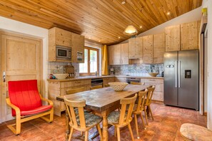 Une cuisine en bois avec une table à manger, des chaises, une chaise rouge, un réfrigérateur et un four à micro-ondes.