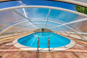 A swimming pool with a glass enclosure, surrounded by a brick patio.