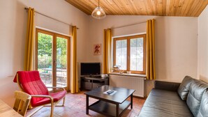 A living room with a sofa, a red chair, a table, a TV, and large windows with curtains. - Orange Riverside House with Shared Pool (Aspiran)