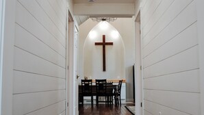 A hallway with wooden flooring and white walls, leading to a dining area with a cross on the wall. - Stay in a Beautifully Restored 1895 Church, A Unique Bear Lake Getaway (Bear Lake)