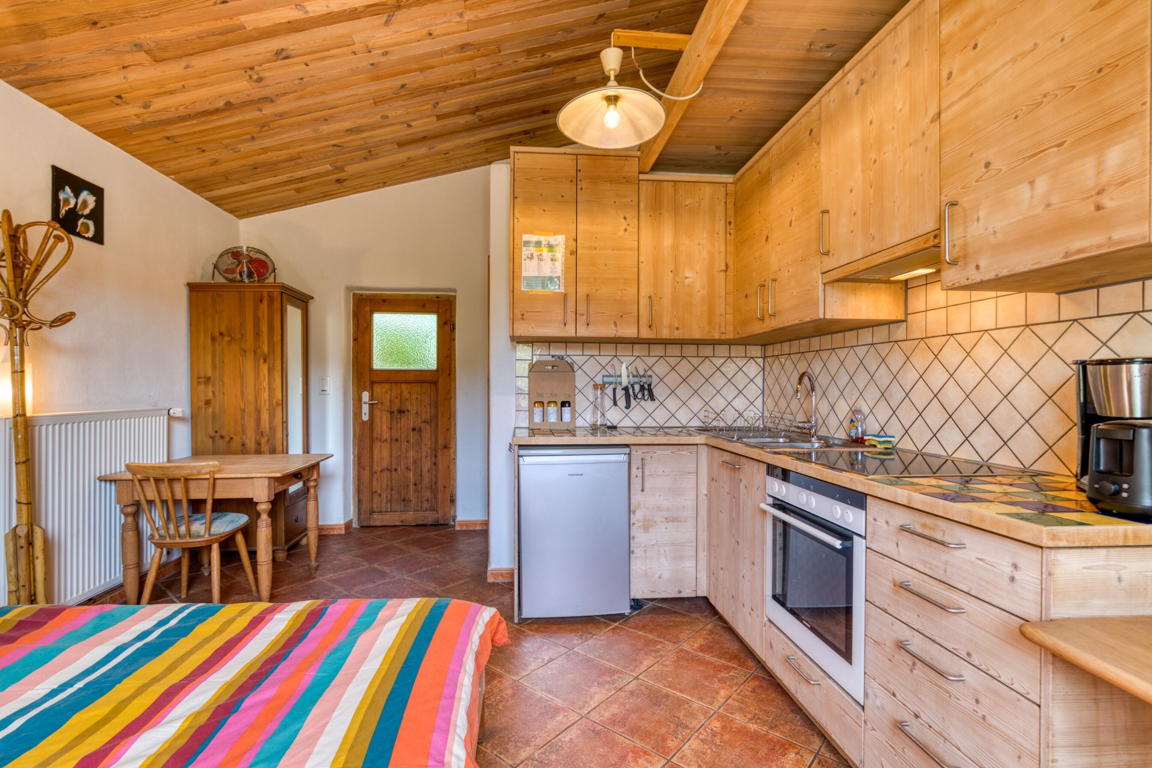 Una cocina con armarios de madera, salpicadero de azulejos, un refrigerador, una estufa y una zona de comedor con mesa y sillas.