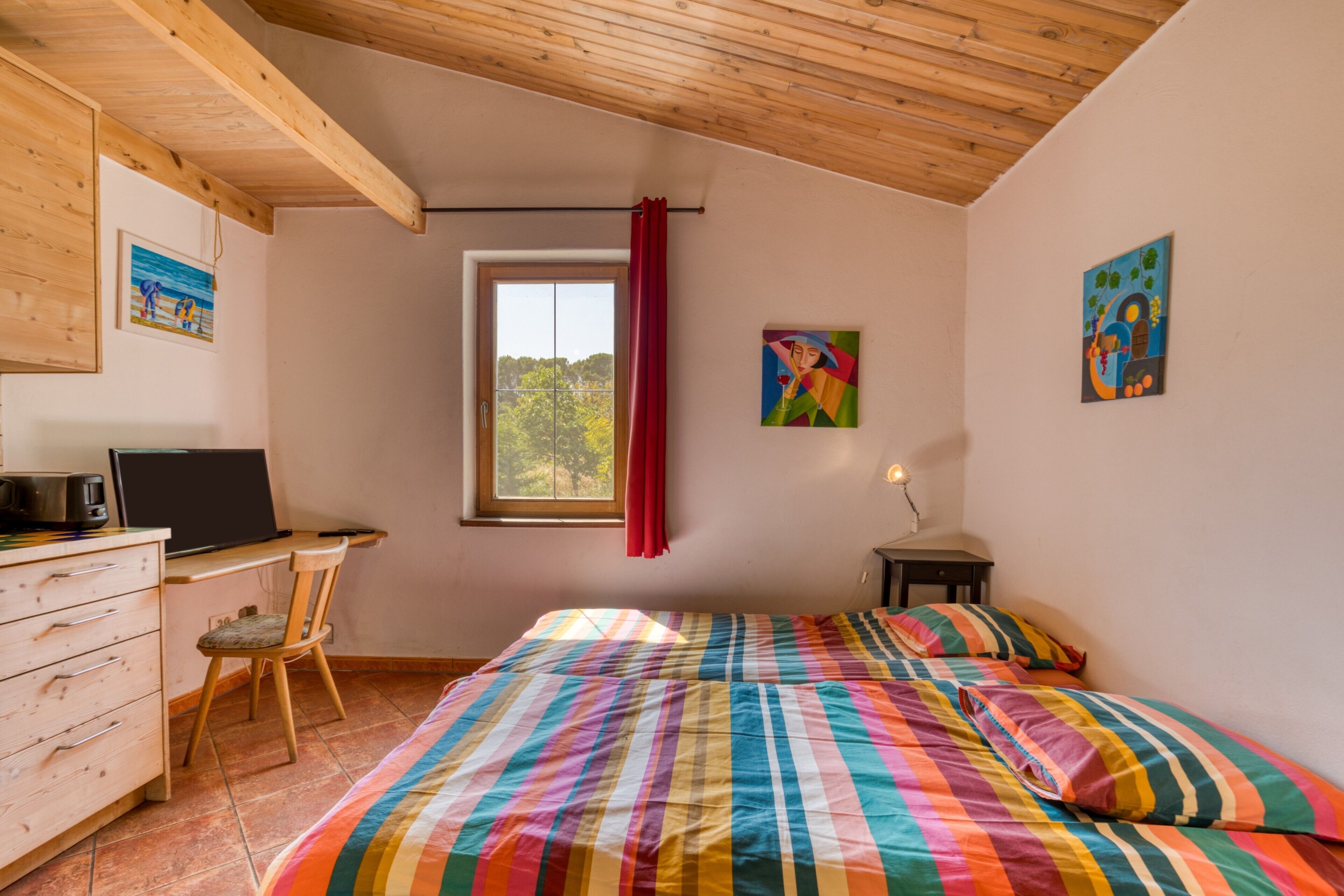 Una camera da letto con un letto, una scrivania, una sedia, una finestra e opere d'arte alle pareti.