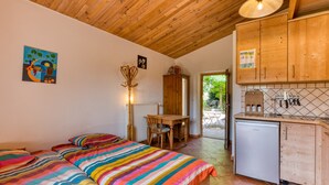 Een slaapkamer met twee bedden, een houten plafond, een klein tafeltje en een kitchenette met houten kastjes en een vaatwasser.